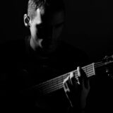 grayscale photo of man playing guitar